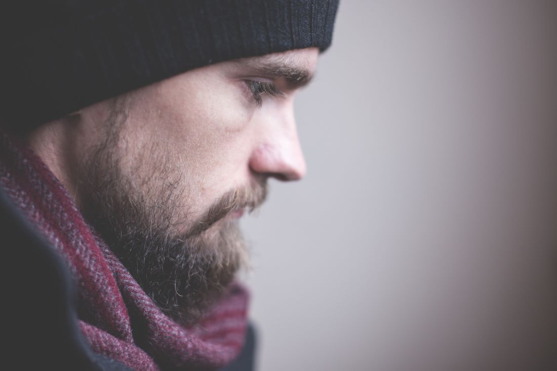 Homem de gorro e cachecol a olhar para o chão
